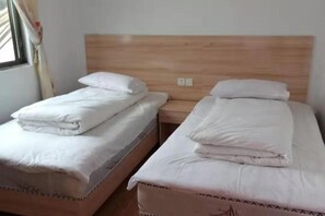 Deux lits simples avec des têtes de lit en bois et du linge de lit blanc dans une chambre.