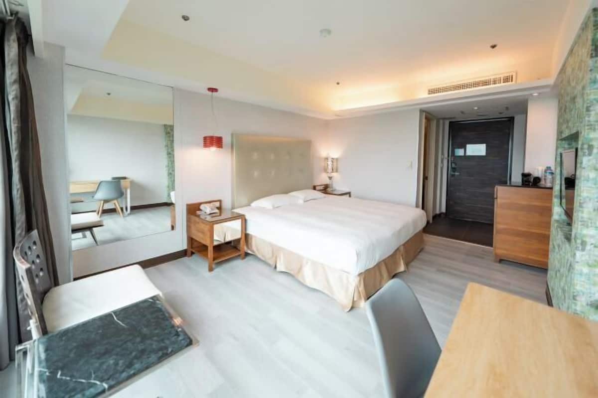 A hotel room with a bed, bedside table, chair, desk, and a mirror.