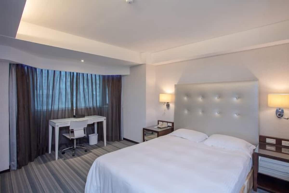 A hotel room with a large bed, a desk, and two bedside lamps.