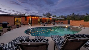 Un área de piscina con sillas de descanso, una parrilla y una zona de estar cubierta con sombrillas.