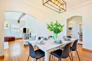A dining area with a white table set for four, black chairs, a green vase with flowers, and a modern chandelier.