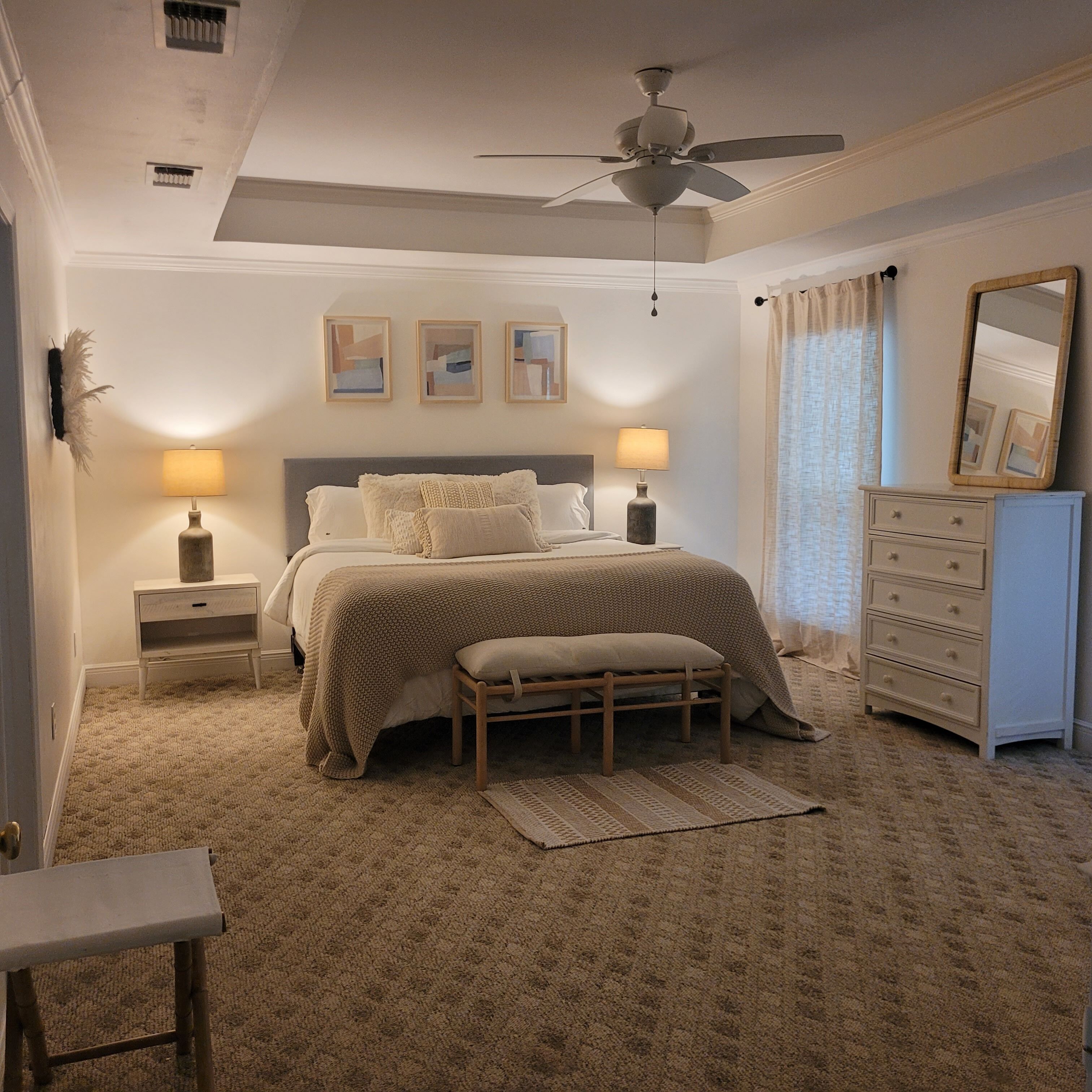 Un dormitorio con cama, lámparas de noche, ventilador de techo, cómoda y espejo.