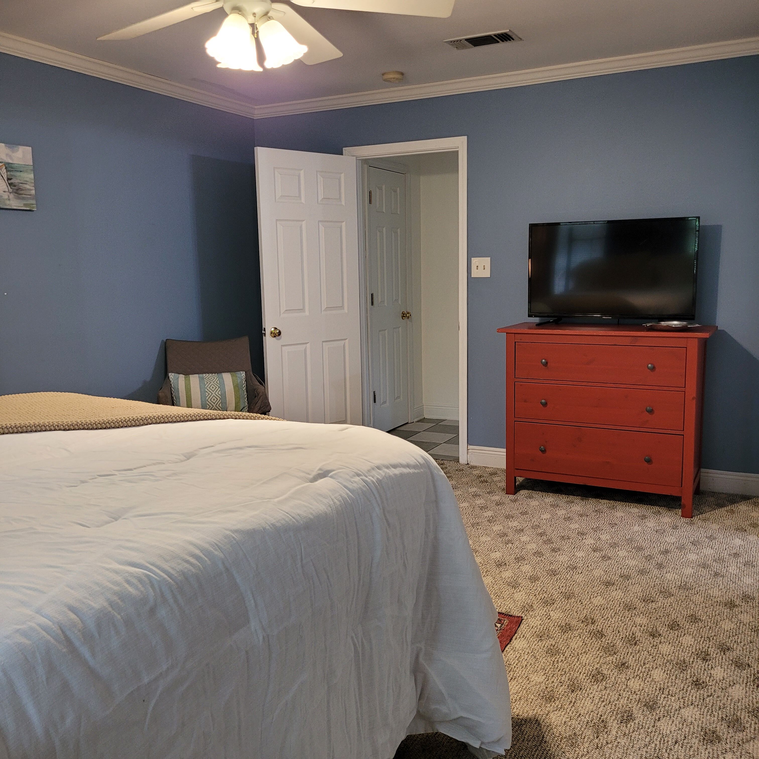 A bedroom with a bed, a dresser, a television, and a door.