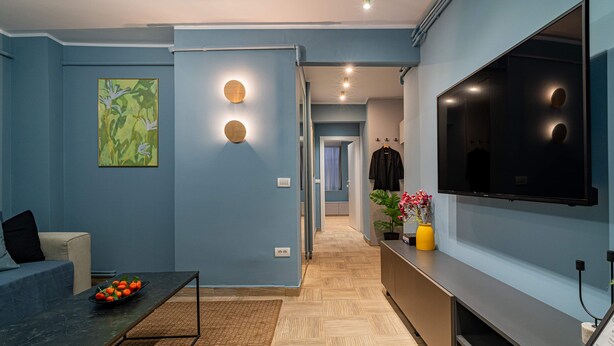 A modern living room with a sofa, coffee table, and a flat-screen TV mounted on the wall. - Lively Colors & Serene Comfort - Renovated 1BR by Piata Universitatii (Bucharest)