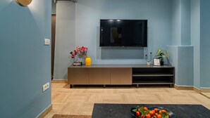 A modern living room with a flat-screen TV mounted on the wall, a wooden entertainment unit below, and a black coffee table with fruit. - Lively Colors & Serene Comfort - Renovated 1BR by Piata Universitatii (Bucharest)