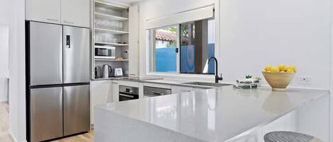 A modern kitchen with a large island, stainless steel appliances, and a view of the sea through a window.