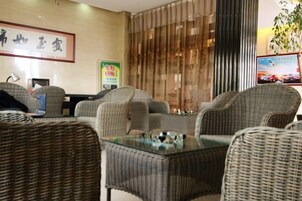 Un hall de hotel con mobiliario de mimbre, una mesa de vidrio y un cartel en la pared.