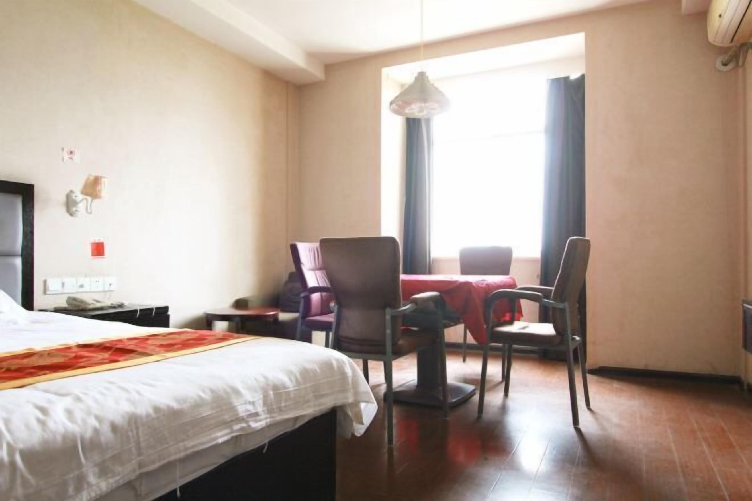 Una camera d'albergo con un letto, una scrivania, due sedie, un tavolo e una finestra con tende.