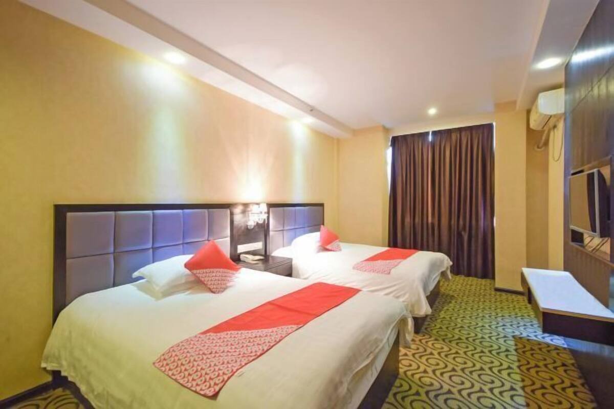 A hotel room with two beds, a bedside table, a desk, and a window with curtains.