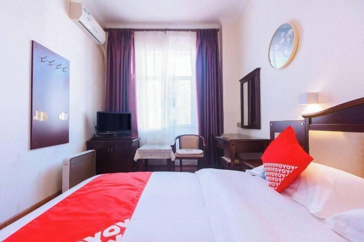 A hotel room with a bed, a desk, a chair, a television, and a window with curtains.