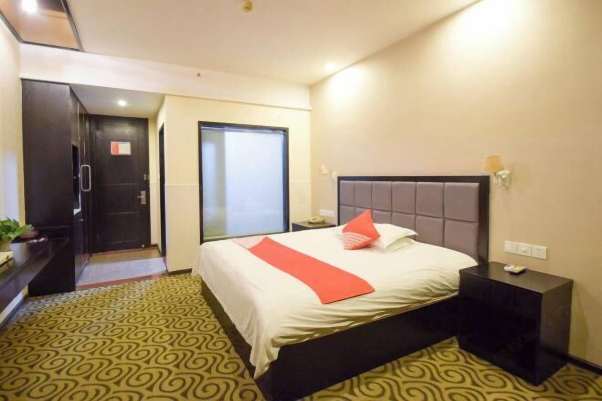 A hotel room with a bed, a nightstand, a door, and a patterned floor.