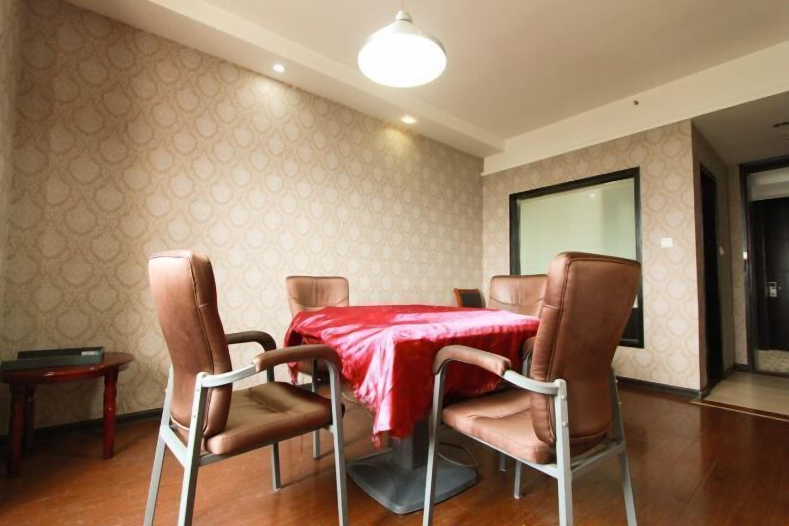 Une salle de conférence avec une table recouverte d’une nappe rouge, entourée de quatre fauteuils en cuir, et une petite table placée sur le côté.