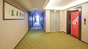 Ein Hotelgang mit einem gemusterten Teppich, einem gerahmten Schild an der Wand und einem Aufzug mit roter Tür.
