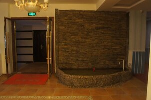 Un vestíbulo con pared de piedra, alfombra roja y una puerta que conduce a otra habitación.