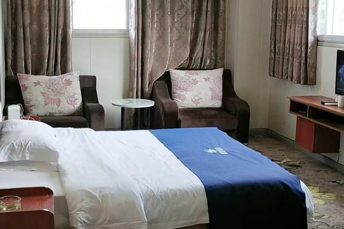 Ein Hotelzimmer mit einem Bett, zwei Sesseln, einem kleinen runden Tisch, einem Fernseher und einem Schreibtisch mit einem Computer.
