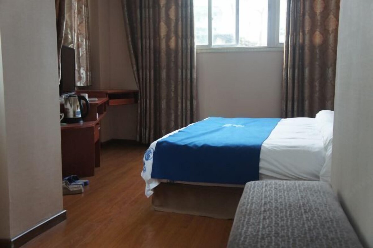 A hotel room with a bed, a desk, a chair, and a window.