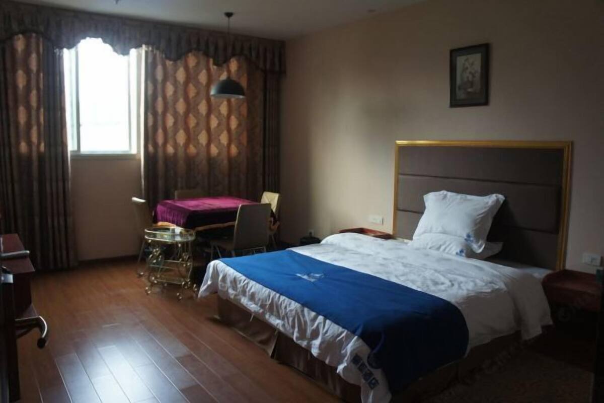 Ein Hotelzimmer mit Bett, Schreibtisch, Stuhl und einem fenster mit Vorhängen.