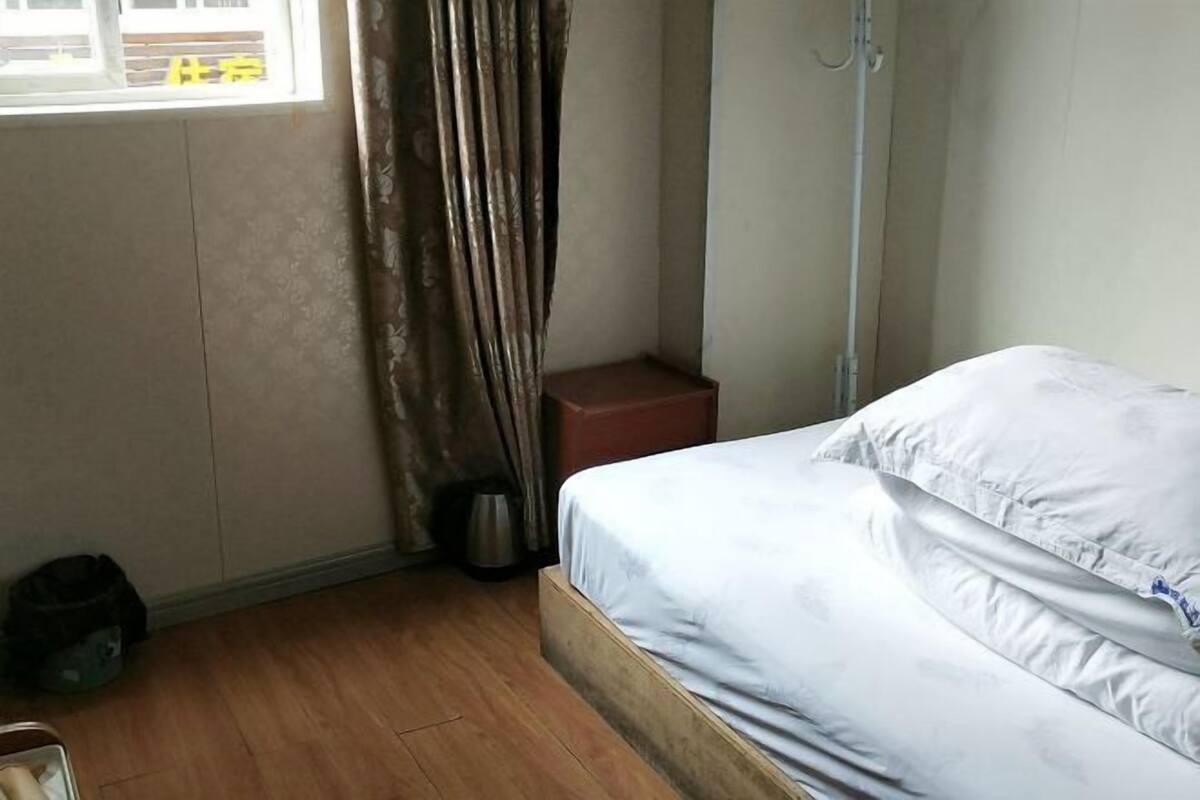 Ein Hotelzimmer mit Bett, Fenster mit Vorhängen, Nachttisch und Mülleimer.