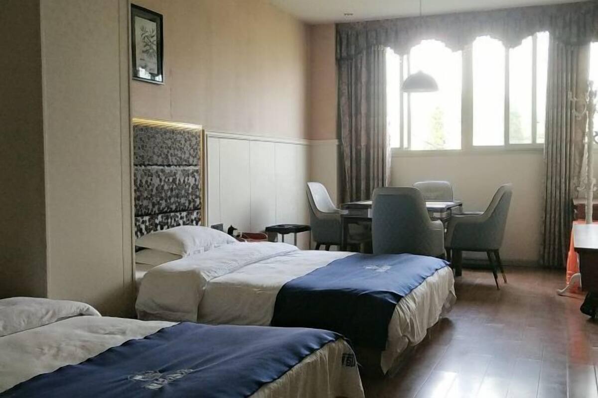 Ein Hotelzimmer mit zwei Betten, einem Schreibtisch, einem Stuhl und einem Fenster mit Vorhängen.