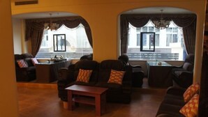 A living room with a sofa set, a coffee table, and a view of a building through large windows. - Lido Hotel (Linshui)