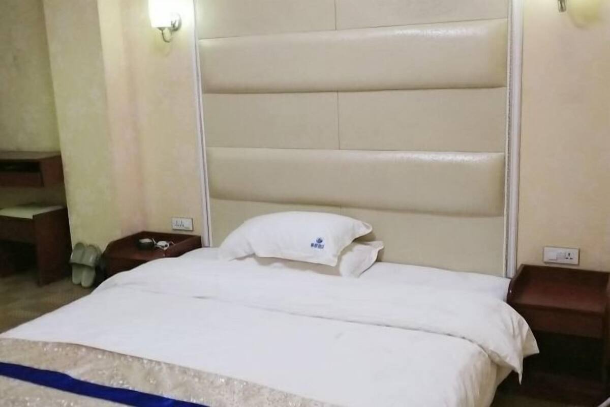 Ein Hotelzimmer mit einem Bett, einem Nachttisch, einer Wandleuchte und einem kleinen Tisch mit Stuhl.