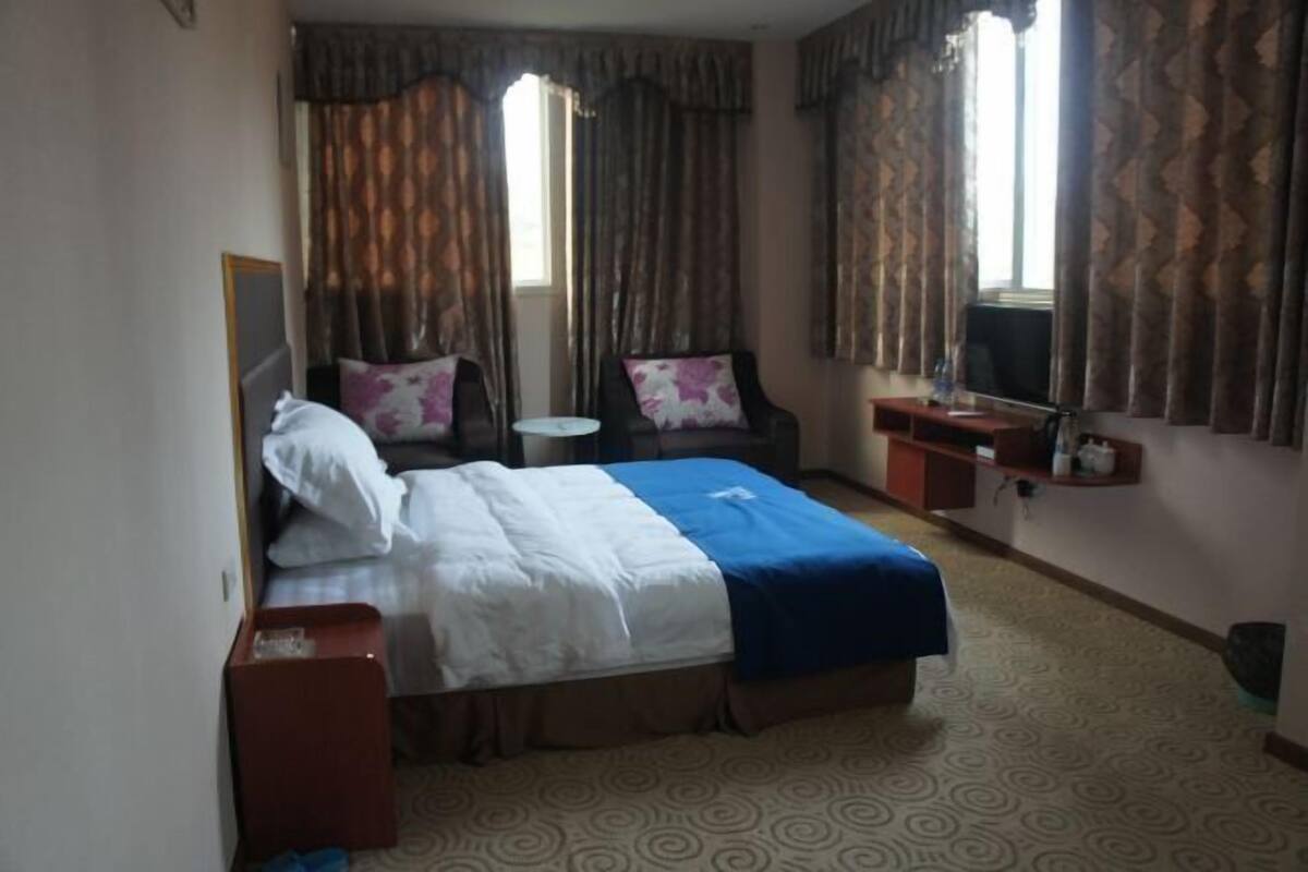 Ein Hotelzimmer mit Bett, Stuhl, kleinem Tisch, Spiegel und Fernseher.