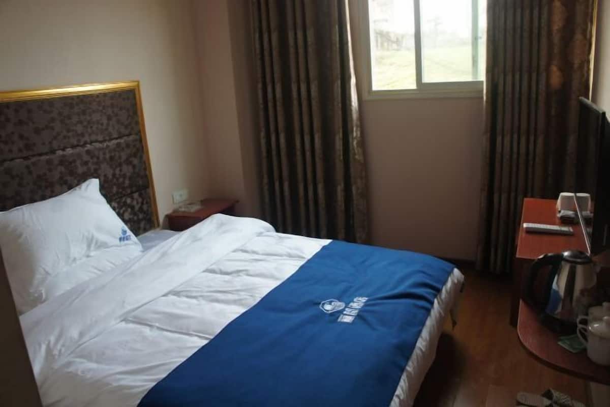 Ein Hotelzimmer mit Bett, einem kleinen Tisch mit Wasserkocher und einem Fenster mit Vorhängen.