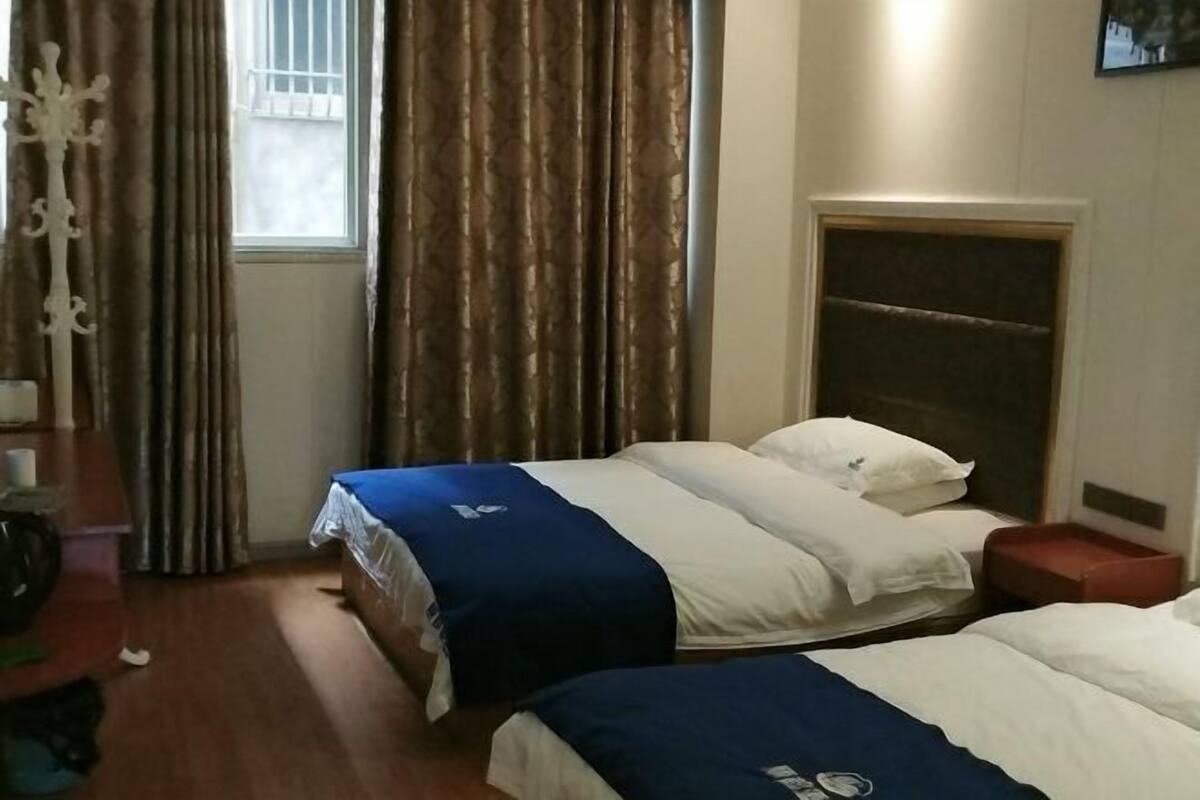 Ein Hotelzimmer mit zwei Betten, Holzboden, einem Fenster mit Vorhängen und einem Kopfteil.