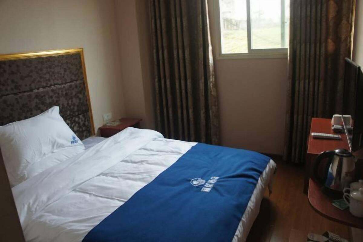 Ein Hotelzimmer mit einem Bett, einem kleinen Tisch mit Wasserkocher, einem Sessel und einem Fenster mit Vorhängen.