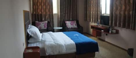 A hotel room with a bed, a chair, a small table, a mirror, and curtains.
