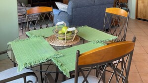 A dining area with a table set for four, surrounded by chairs. A television is mounted on the wall to the left.