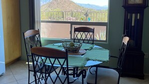 A dining area with a table set for four, chairs, a chandelier, a clock, and a view of a mountain.