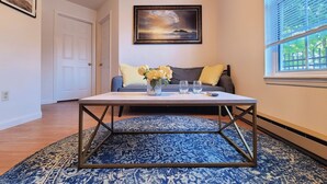 A room with a sofa, a coffee table with a vase of flowers, and a painting on the wall. - Safe & Secure 2br near UKPD in Lex - Rest easy, walk 2 UK (Lexington)