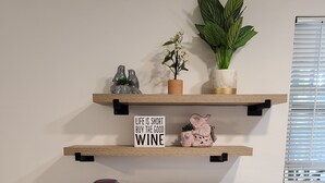 A kitchen counter with a microwave, coffee maker, and various dishes. There are two shelves above the counter with decorative items and a sign that says "Life is short, buy the good wine." - Safe & Secure 2br near UKPD in Lex - Rest easy, walk 2 UK (Lexington)