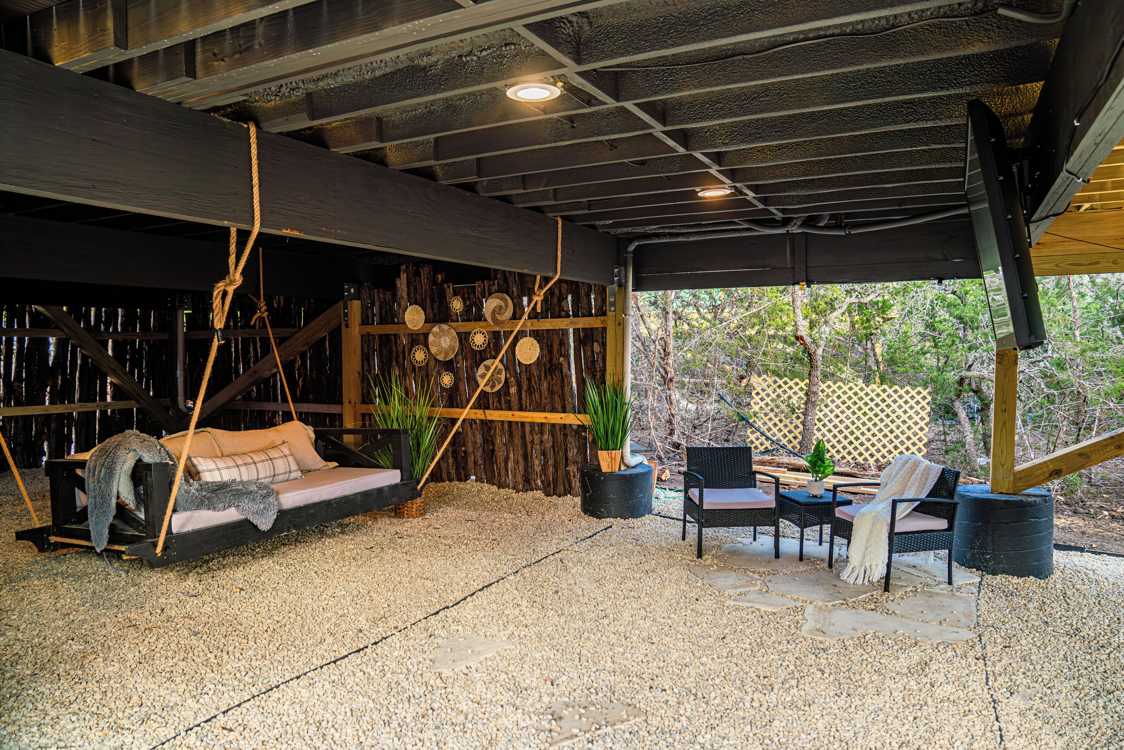 A covered outdoor seating area with a swing, wicker chairs, and a stone floor.
