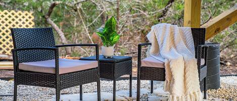 Two wicker chairs with cushions, a small table with a potted plant, and a wooden deck with a lattice fence in the background.