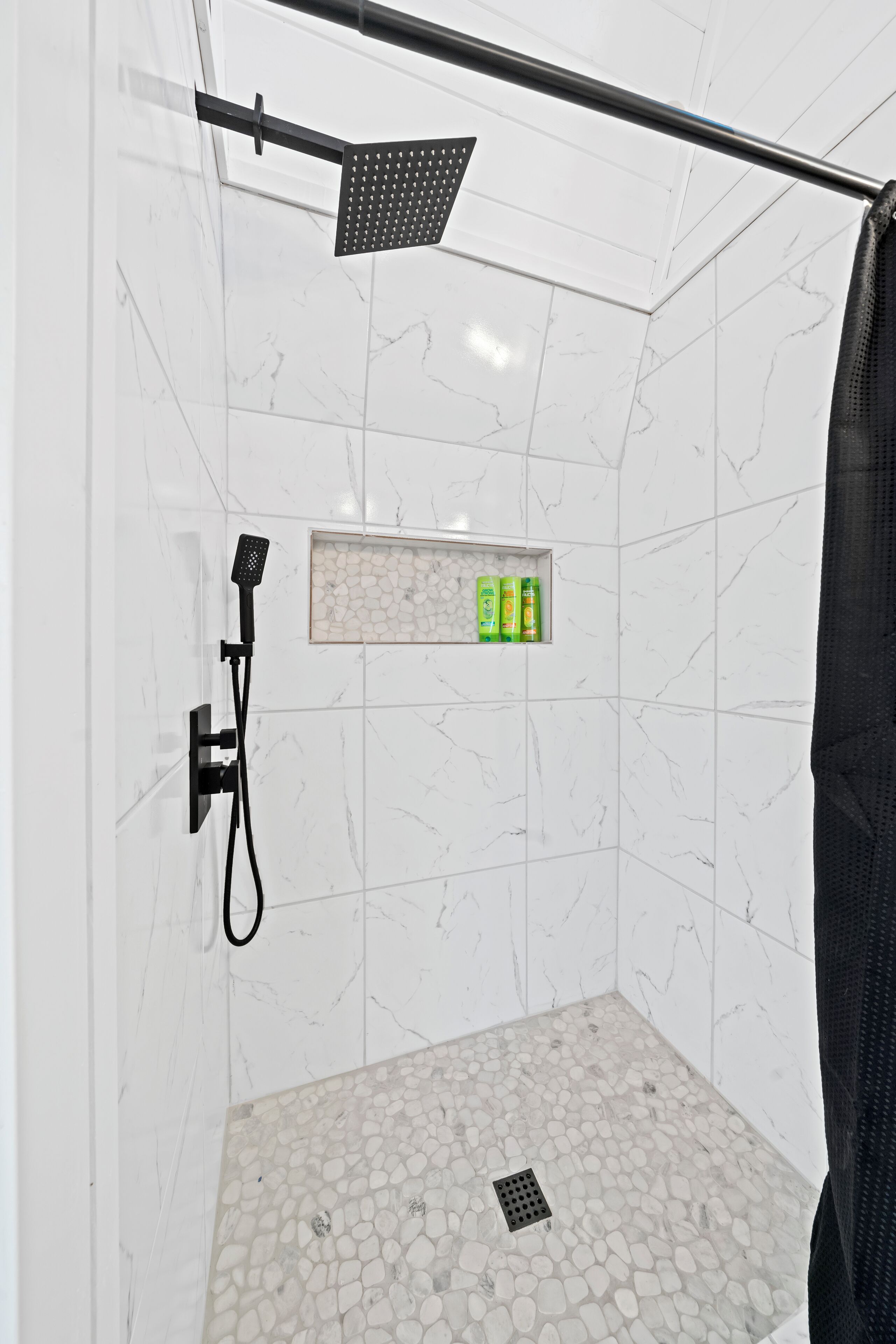 A shower area with a handheld showerhead, a built-in shelf with toiletries, and a pebble-patterned floor.