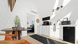 Ett modernt kök med vita skåp, ett svart kylskåp, en mikrovågsugn och en diskho. Det finns en matplats med ett runt bord och orange stolar.
