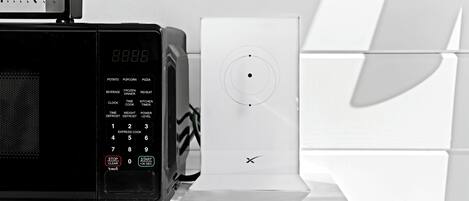 A black microwave with a digital clock and a white appliance with a circular dial, both on a white tiled countertop.