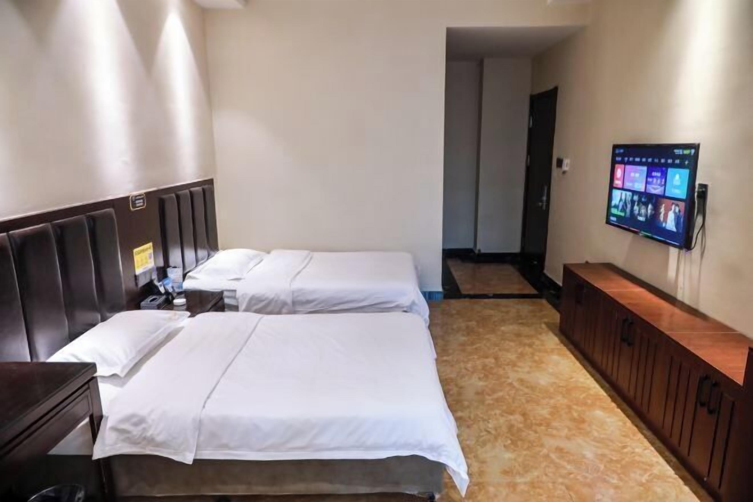 A hotel room with two beds, a TV mounted on the wall, and a wooden cabinet.