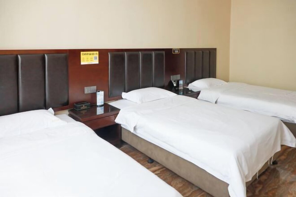 A hotel room with three single beds, wooden headboards, and a small bedside table with a lamp.