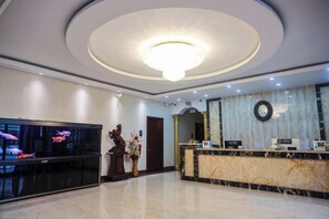 A hotel lobby with a reception desk, a large chandelier, and a television screen.
