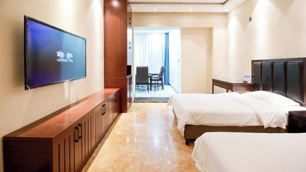 A hotel room with a TV, two beds, a wooden cabinet, and a view of the outside.