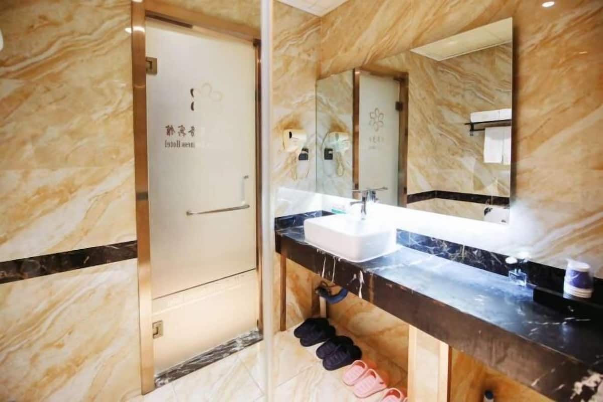 Une salle de bain avec un sol en marbre, un lavabo blanc et un miroir au-dessus. On peut voir des chaussons suspendus à un porte-chaussons situé sous le lavabo.