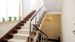 A staircase with a metal railing, potted plants on the landing, and a chandelier on the wall.