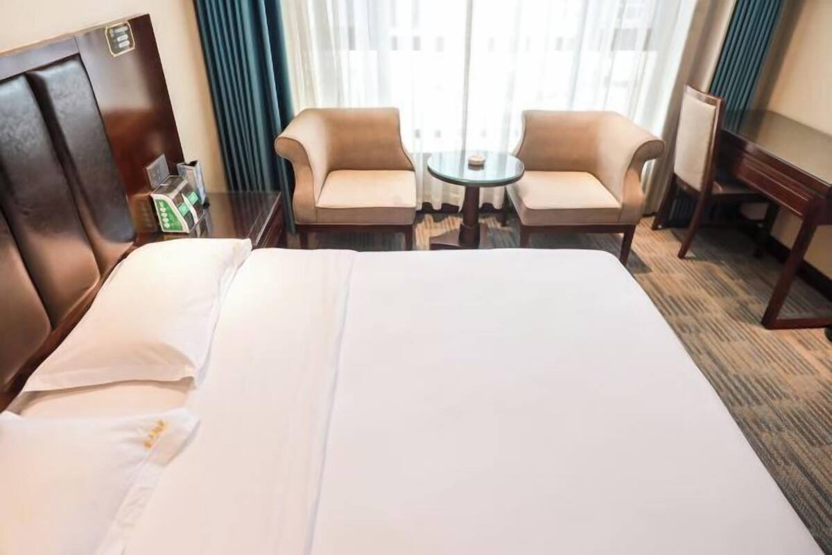 Une chambre d’hôtel avec un lit, deux fauteuils, une petite table et une table de chevet.