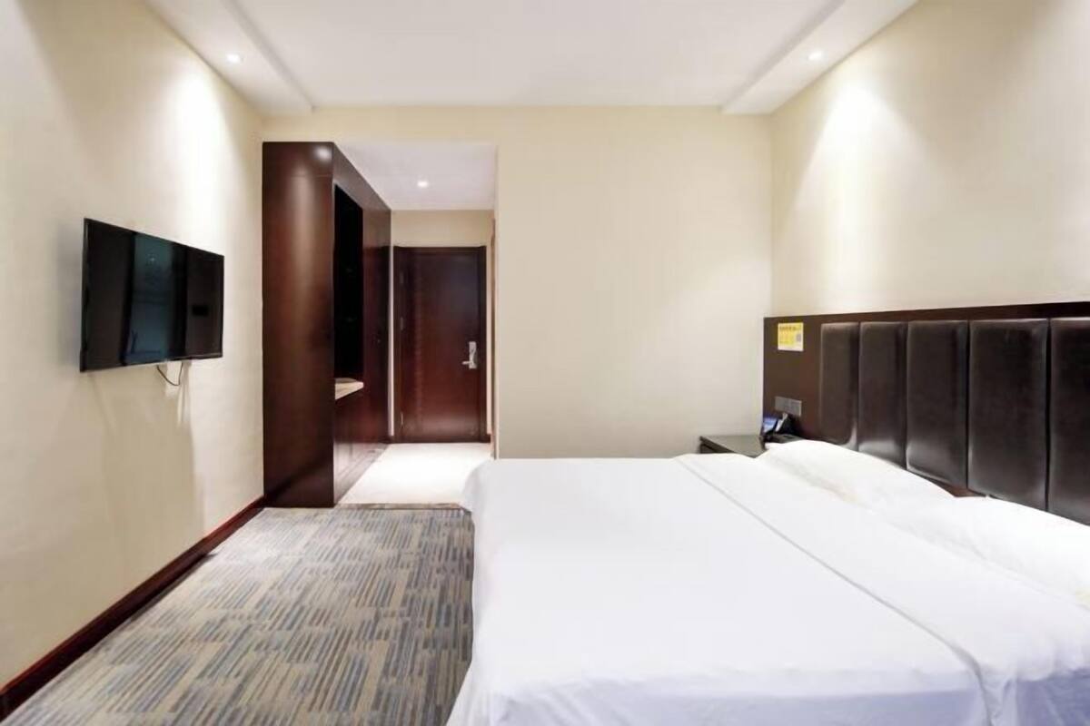 Une chambre d’hôtel avec un lit, un téléviseur à écran plat fixé au mur, une porte en bois et un sol recouvert de moquette.