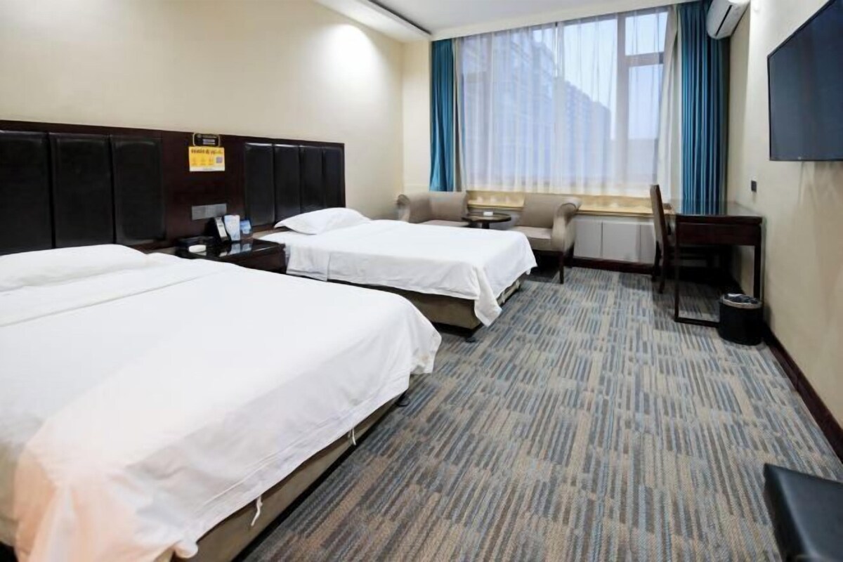A hotel room with two beds, a sofa, a desk, and a TV.