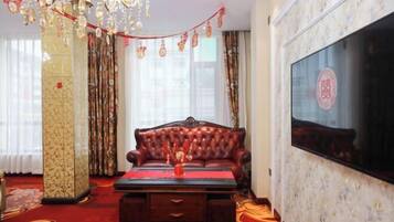 Una habitación con alfombra roja, un sofá de cuero, una mesa de centro de madera, una araña y un televisor grande en la pared.