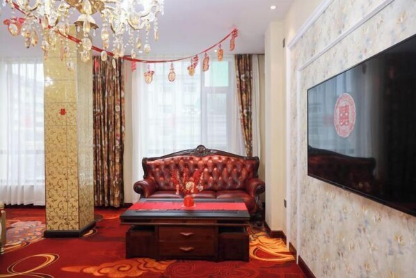 A room with a red carpet, a leather sofa, a wooden coffee table, a chandelier, and a large TV on the wall. - Changchun Golden Sunshine Business Hotel (Changchun)
